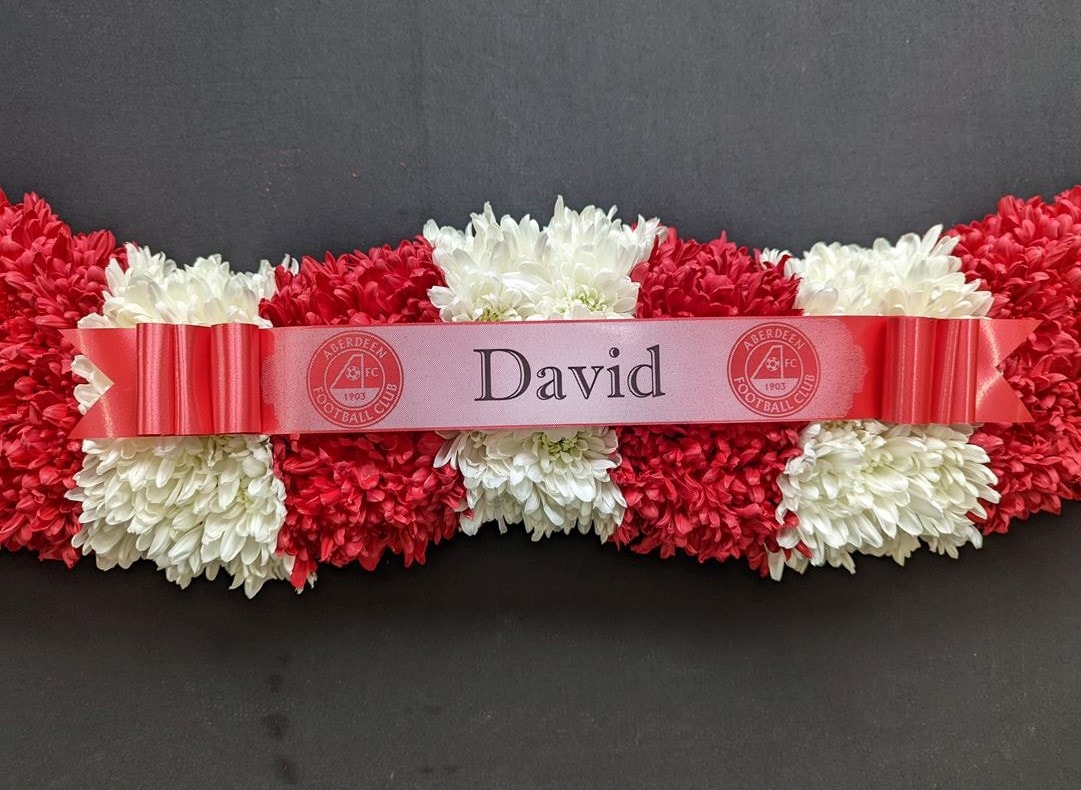 Red and white funeral tribute in the shape of a football scarf – side view