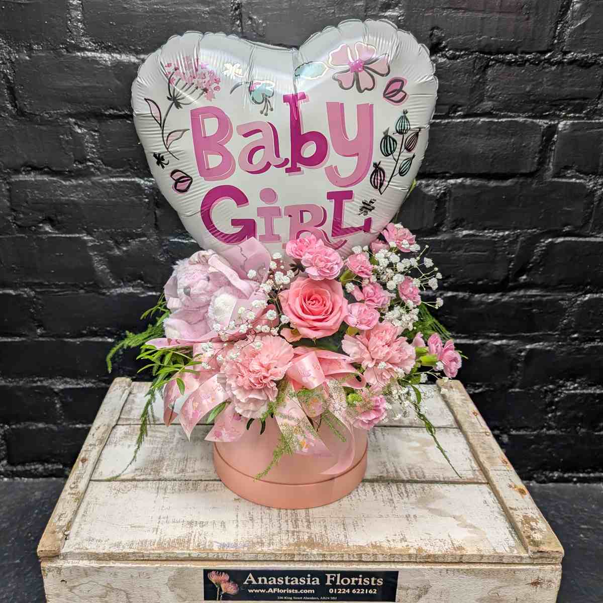 “Baby Girl” new baby gift with heart balloon, pink teddy bear and pink flower arrangement in a blush hat box on a wooden crate – Anastasia Florists Aberdeen - Open View