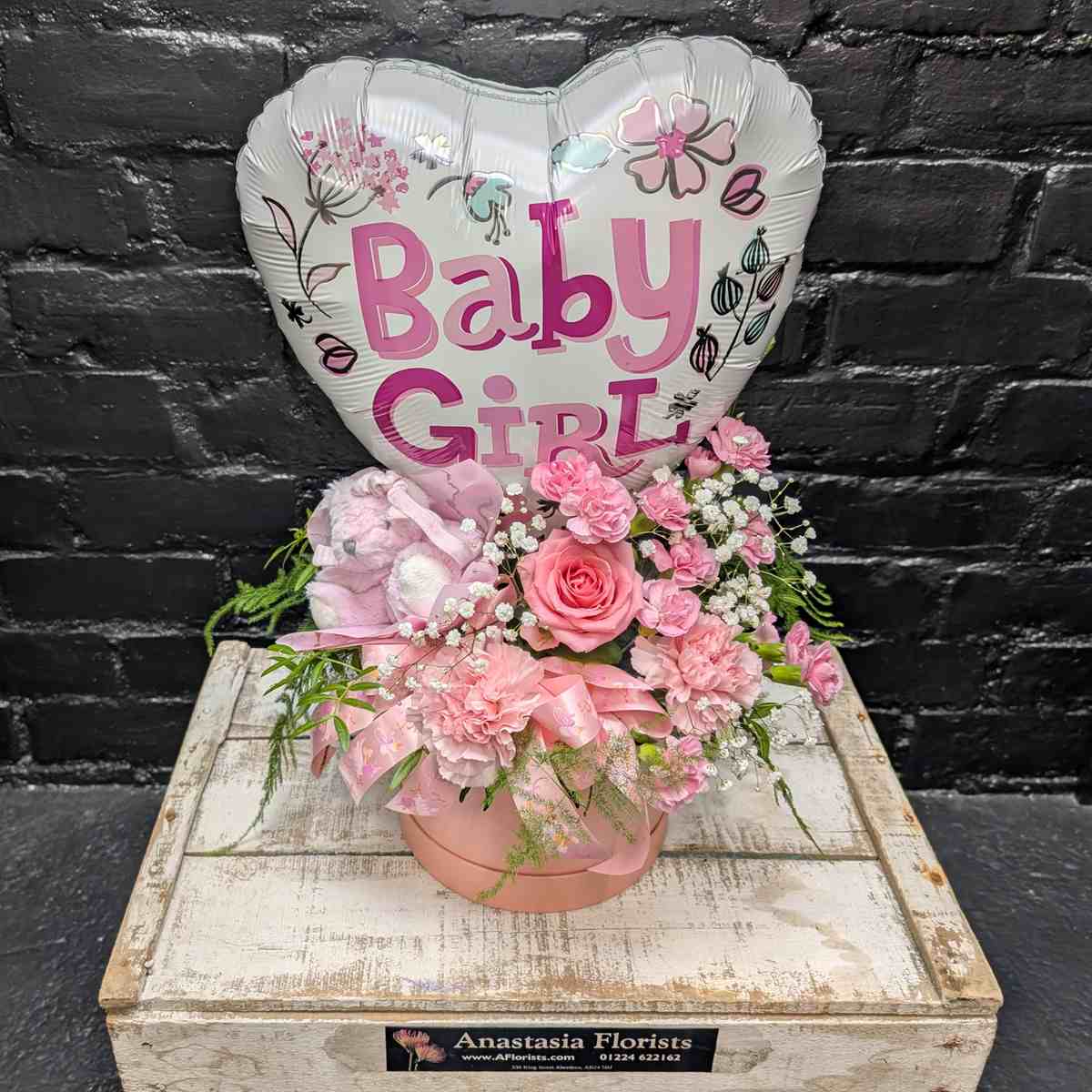 “Baby Girl” new baby gift with heart balloon, pink teddy bear and pink flower arrangement in a blush hat box on a wooden crate – Anastasia Florists Aberdeen - Far View