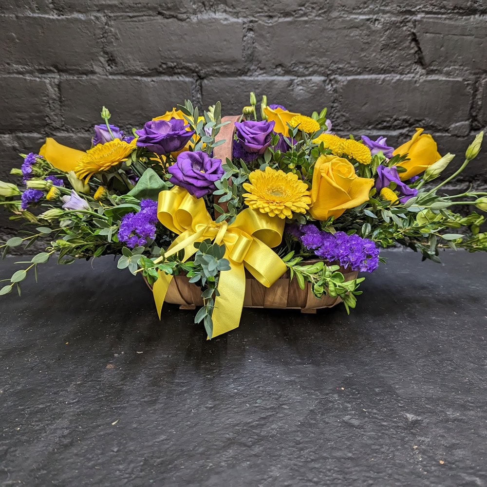 Vibrant arrangement of fresh seasonal flowers in a rustic woven basket, perfect for a cheerful gift or sympathy. - Angle view