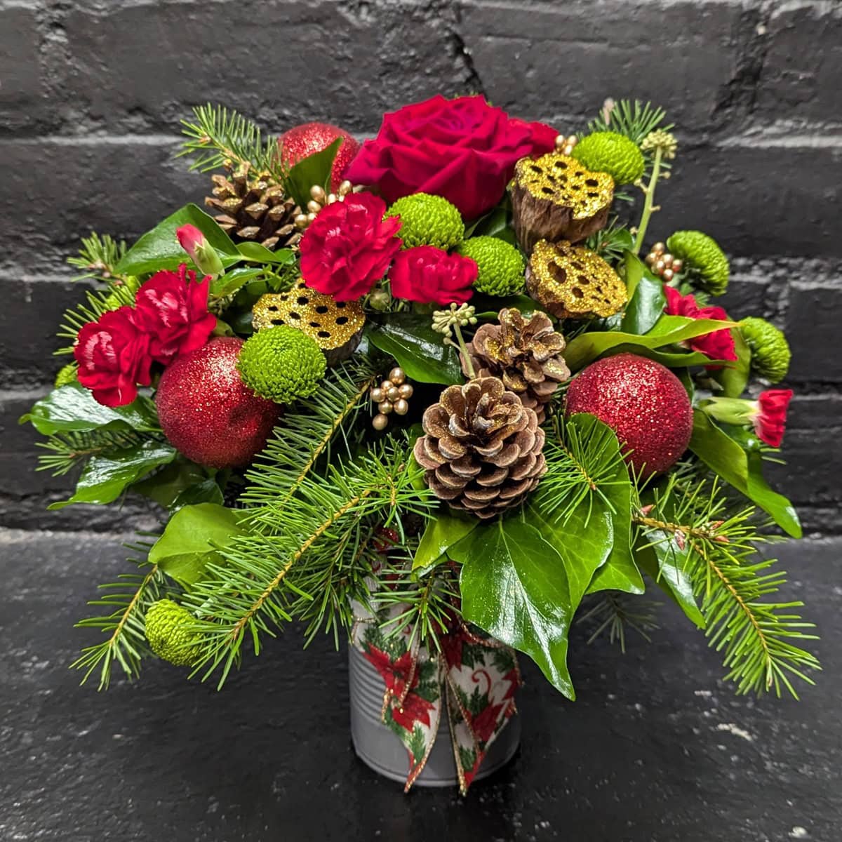 Red and green Christmas floral arrangement in a tin