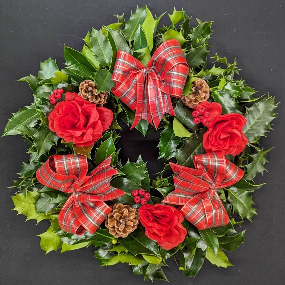 Holly graveside Christmas wreath with red tartan bows, red rose accents, pinecones and red berries