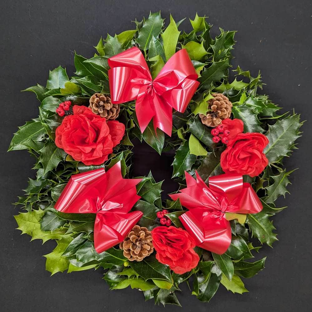 Holly graveside Christmas wreath with red bows, red rose accents, pinecones and red berries