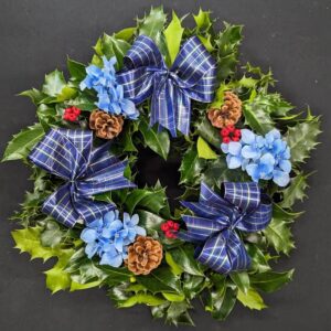 Holly graveside Christmas wreath with navy tartan bows, blue floral accents, pinecones and red berries