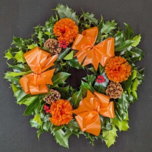 Holly graveside Christmas wreath with orange bows, orange flower accents, pinecones and red berries