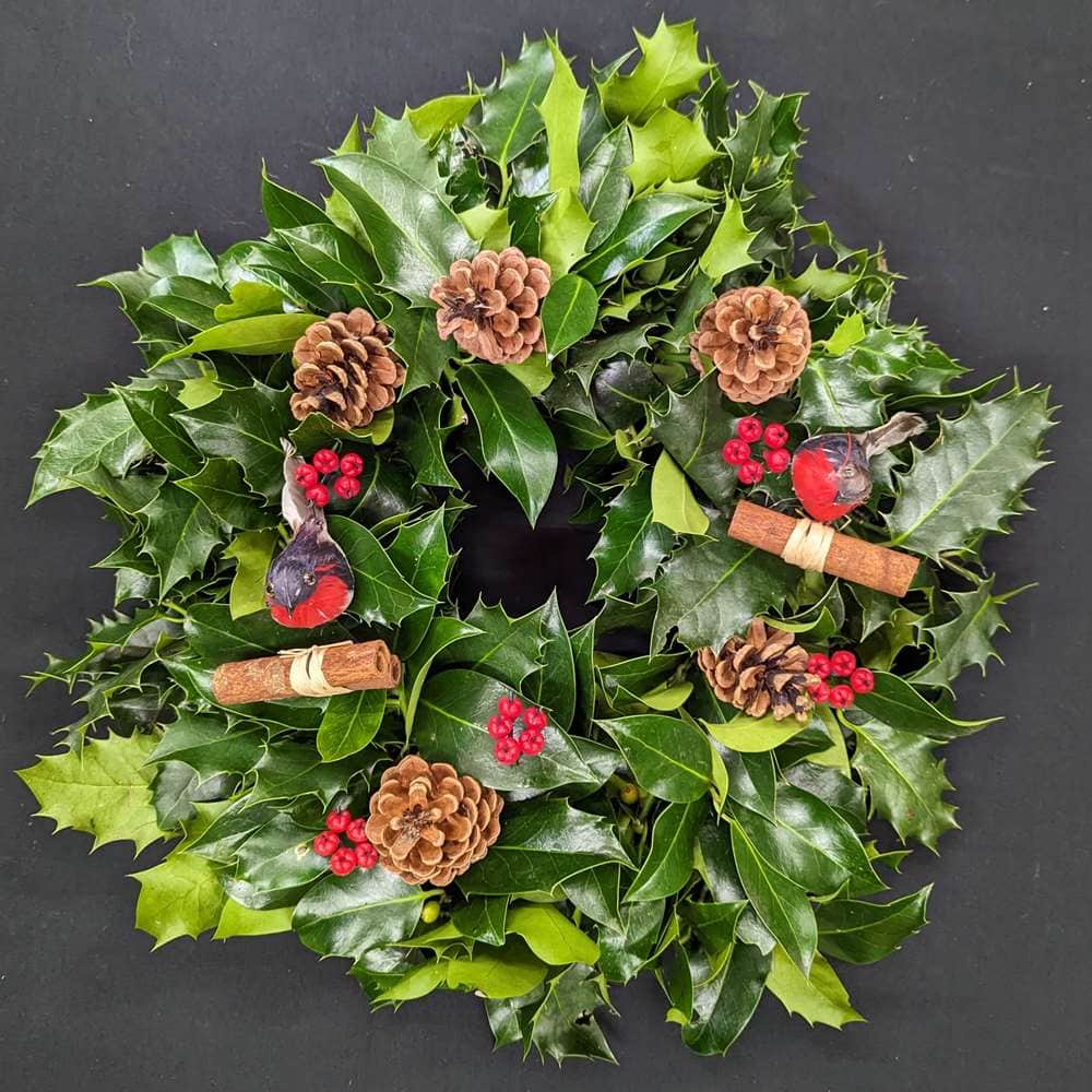 Holly graveside Christmas wreath with robin decorations, pinecones, red berries and cinnamon