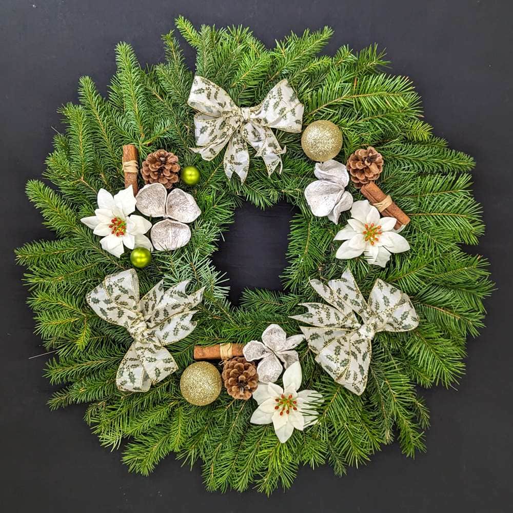 White and silver pine Christmas door wreath with white bows, poinsettia, pinecones and gold baubles