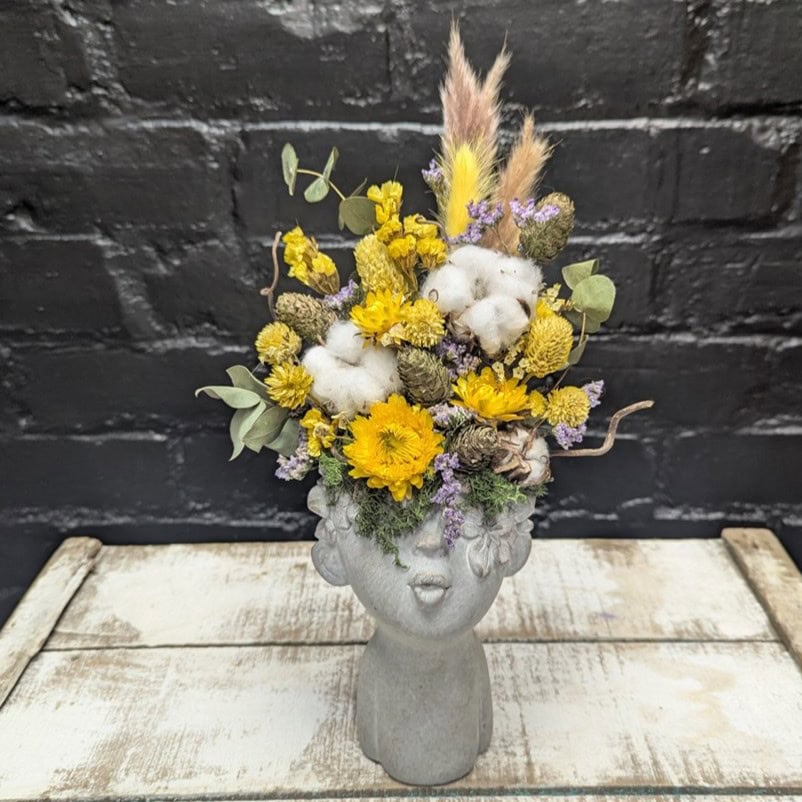 Bright dried flower face vase arrangement with yellow blooms, cotton, grasses and preserved foliage in a stone-style head vase – Anastasia Florists Aberdeen - Angle View