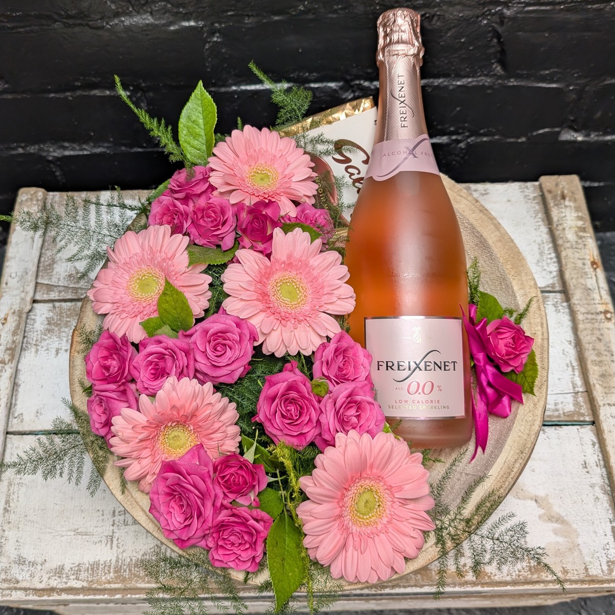 Pink flowers arranged in a wooden bowl with a bottle of sparkling drink. – close-up