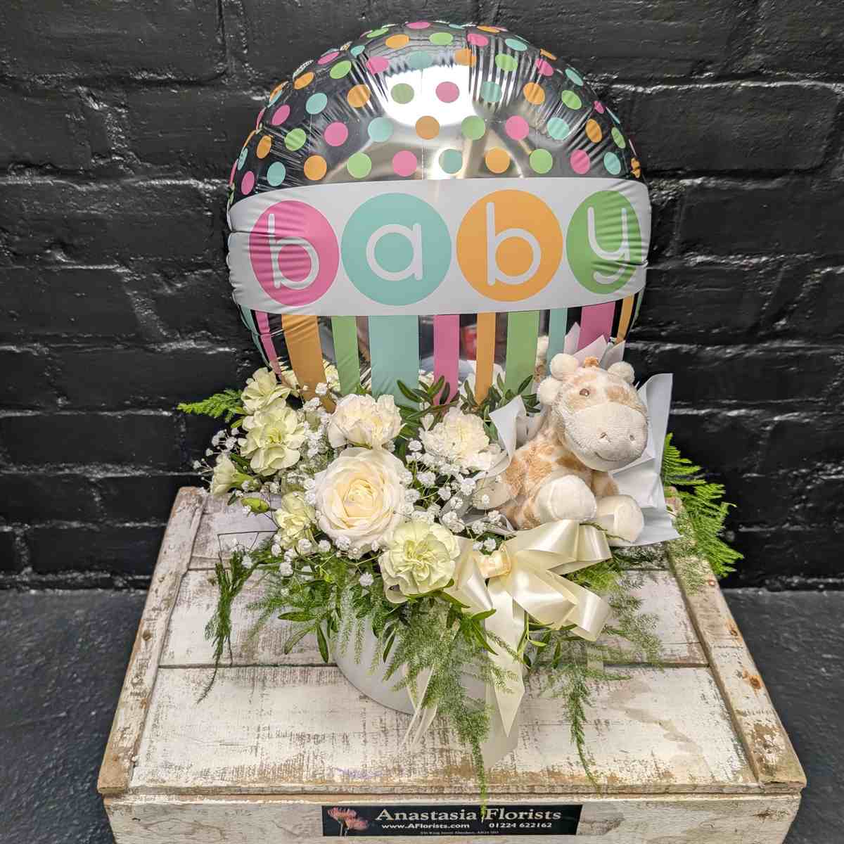 New baby gift with colourful “Baby” balloon, soft toy and cream and white flower arrangement in a white hat box on a wooden crate – Anastasia Florists Aberdeen - Side View