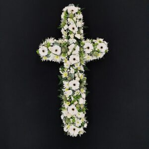 All white funeral cross with gerberas, chrysanthemums and greenery on dark background