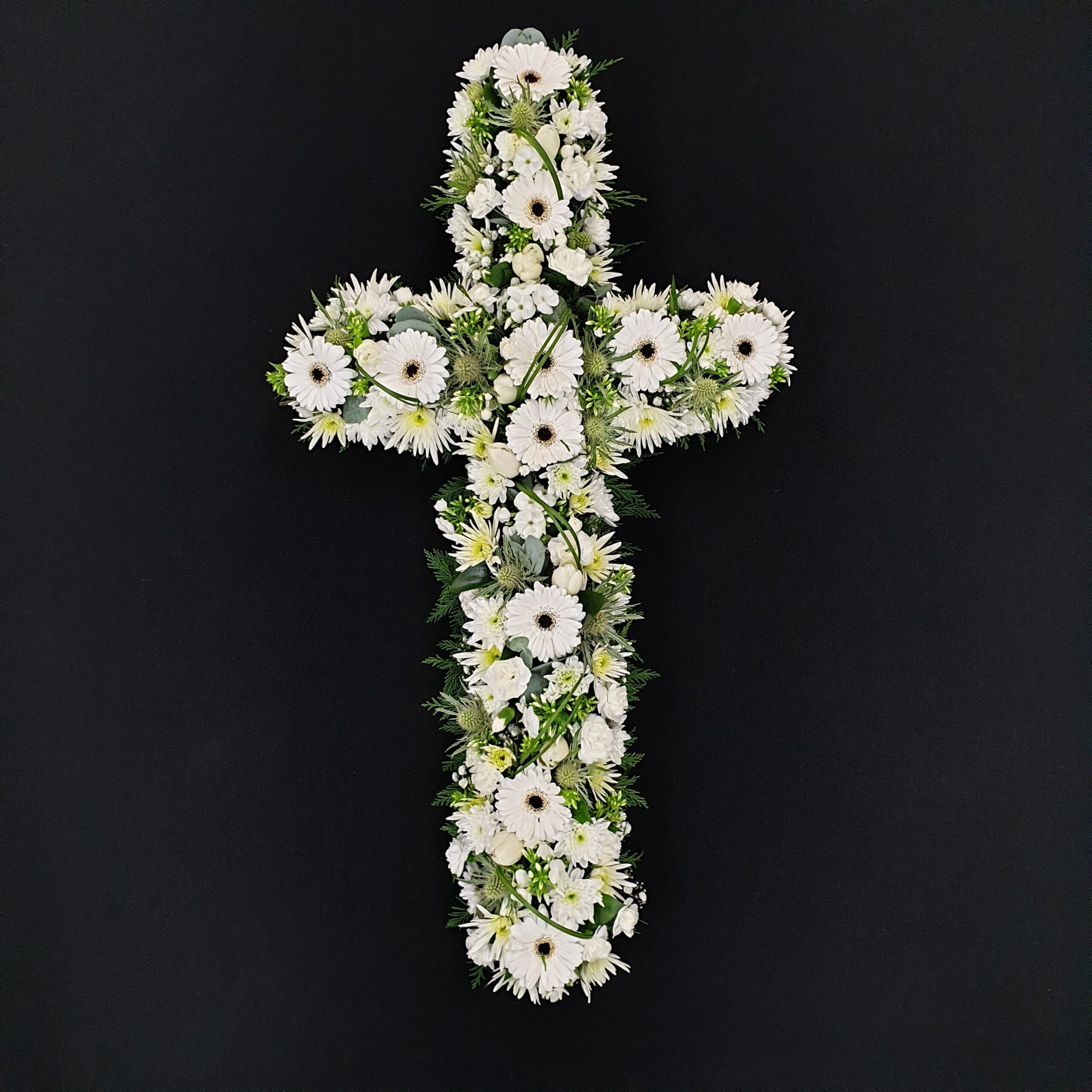 All white funeral cross with gerberas, chrysanthemums and greenery on dark background