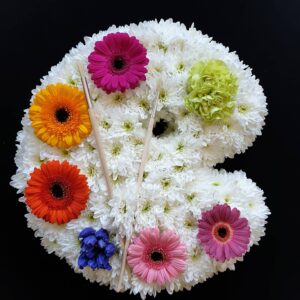 Artist palette funeral tribute with white chrysanthemums, colourful flowers and paintbrushes