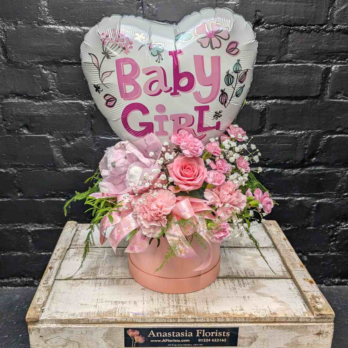 “Baby Girl” new baby gift with heart balloon, pink teddy bear and pink flower arrangement in a blush hat box on a wooden crate – Anastasia Florists Aberdeen