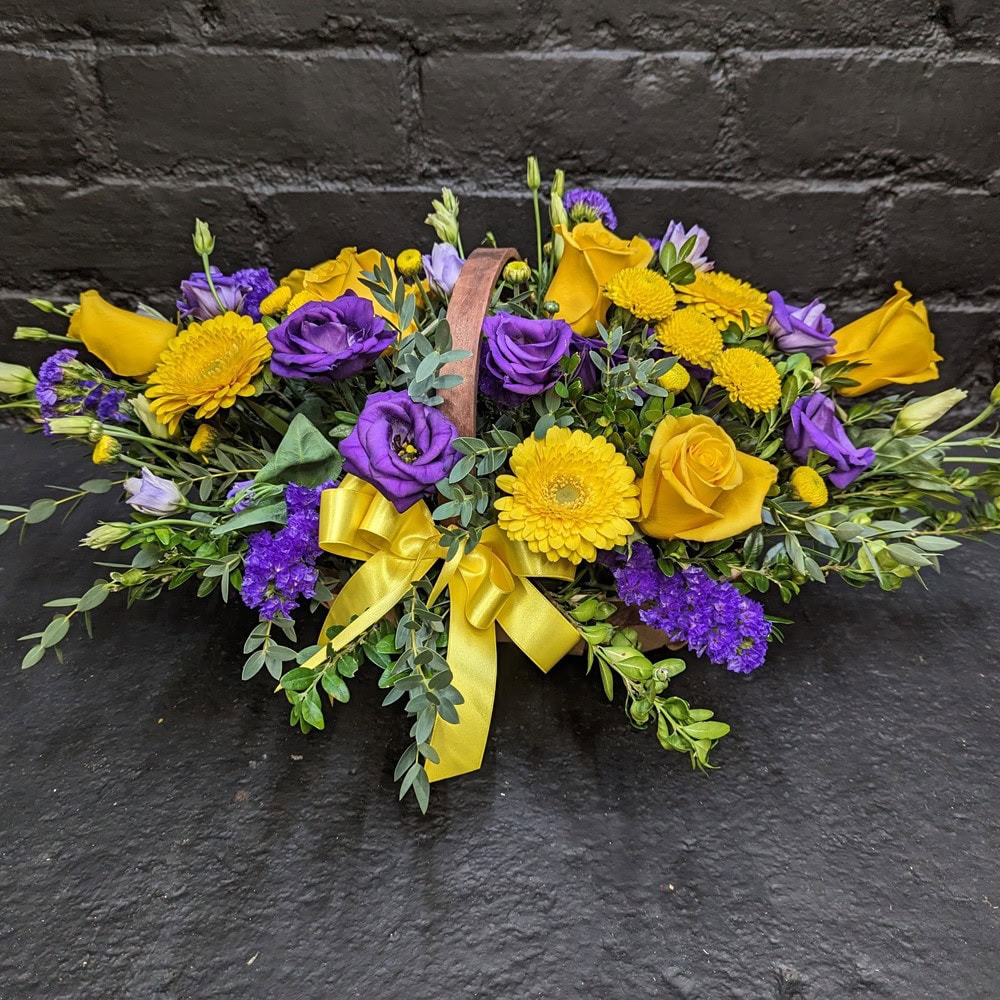 Vibrant arrangement of fresh seasonal flowers in a rustic woven basket, perfect for a cheerful gift or sympathy.