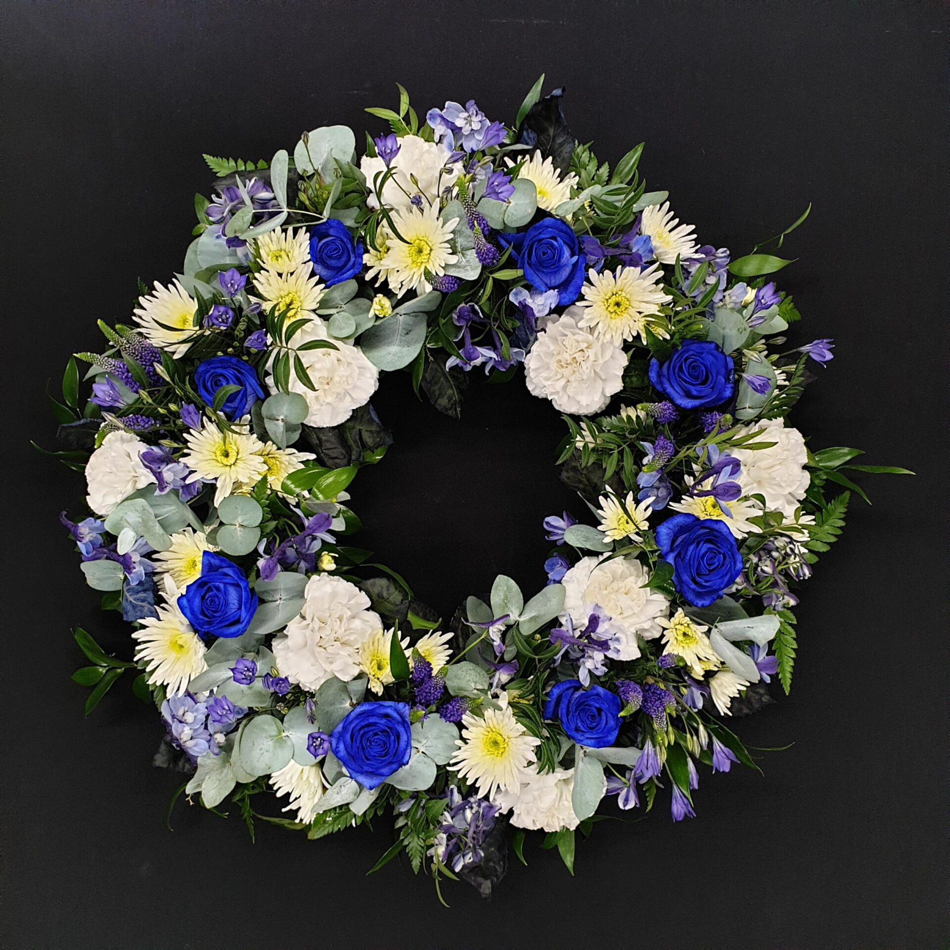 Blue and white funeral wreath with blue roses, white carnations and eucalyptus