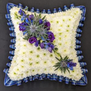 Blue tartan funeral cushion tribute with white chrysanthemum base and purple thistle spray