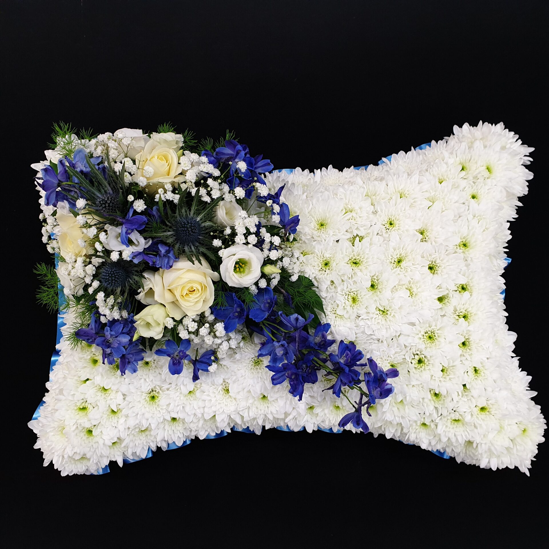 Blue and white funeral pillow tribute with ivory roses and white chrysanthemum base