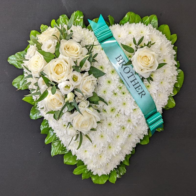 White chrysanthemum heart funeral tribute with white roses, green leaf collar and teal Brother ribbon on a dark background