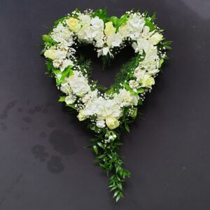 White and green open heart funeral tribute with roses, hydrangea and trailing foliage on a dark background