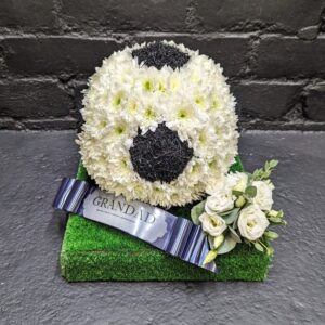 Football funeral tribute with flower-covered football and grass base