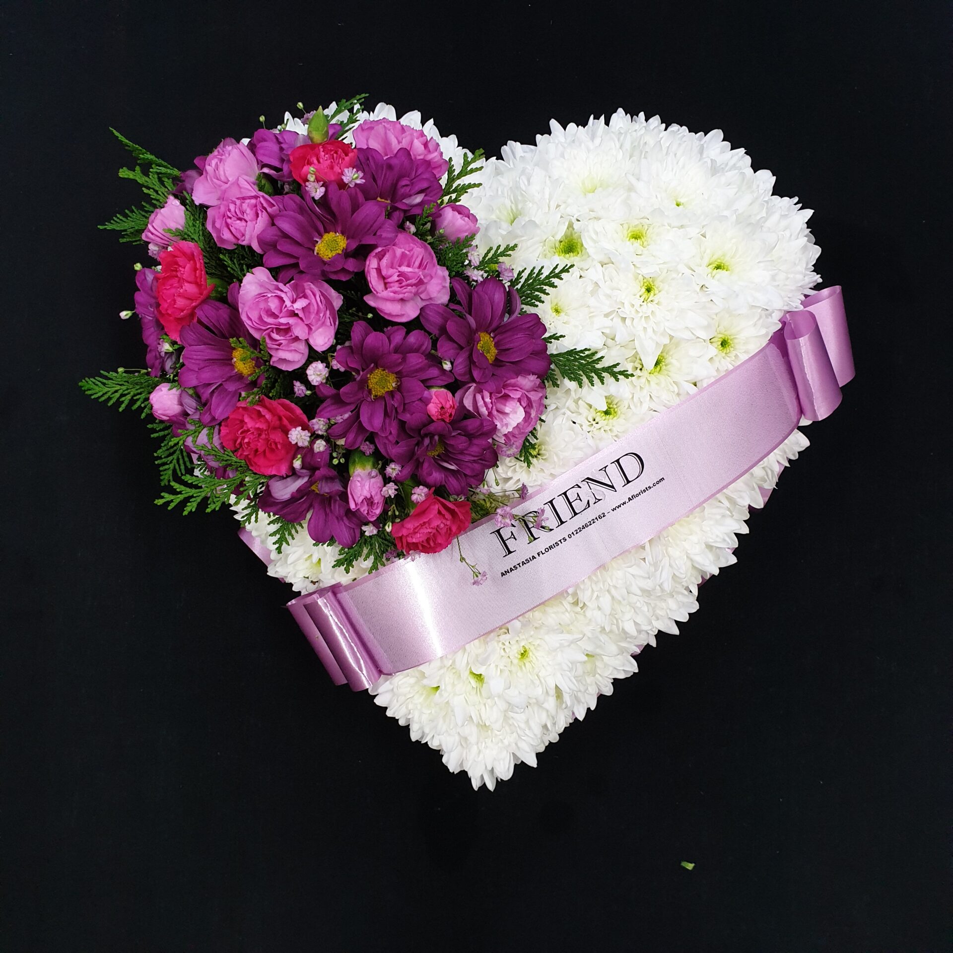 White chrysanthemum heart funeral tribute with purple and pink flowers and Friend ribbon on a black background