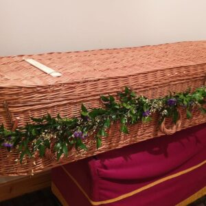 Natural coffin garland on wicker coffin with trailing greenery