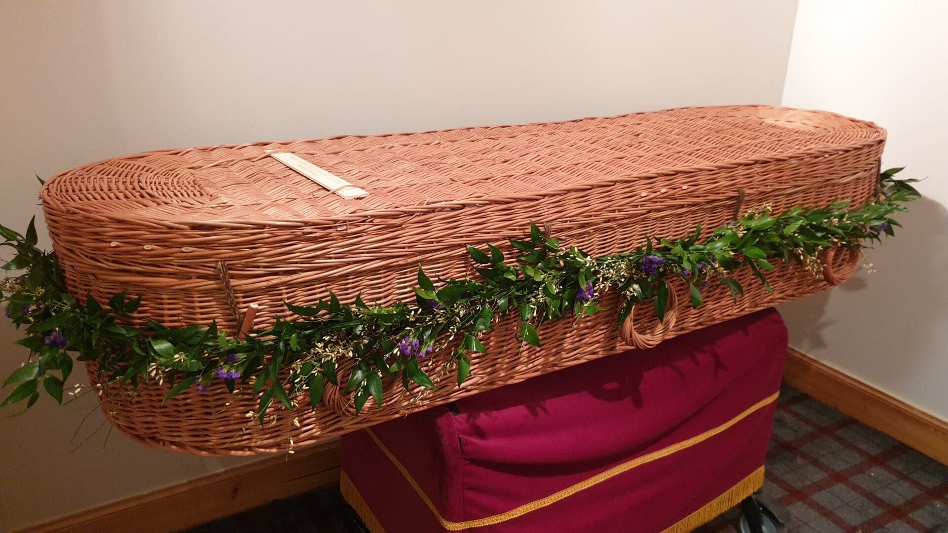 Natural coffin garland on wicker coffin with trailing greenery