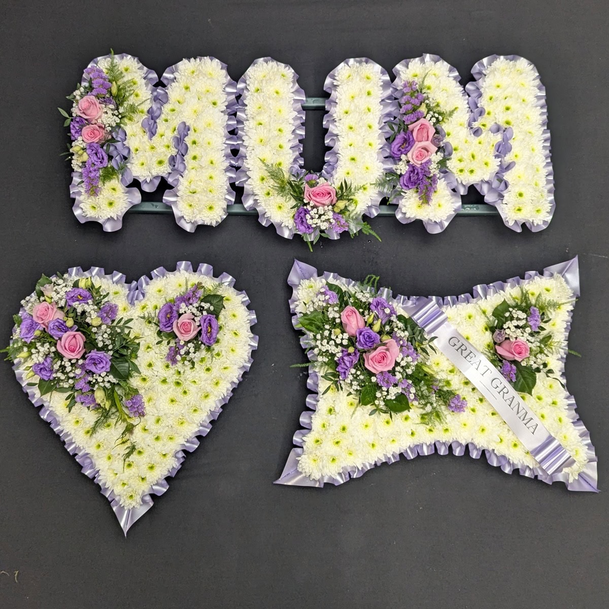 MUM letter, heart and cushion funeral tribute set in white chrysanthemums with lilac ribbon edging and pink and purple flower sprays.