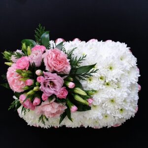 Miniature white chrysanthemum funeral pillow with soft pink carnations, lisianthus and greenery on a black background