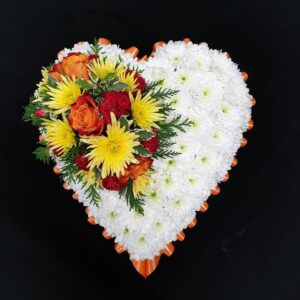 Orange and yellow heart funeral tribute with white chrysanthemum base and orange ribbon edging on a black background