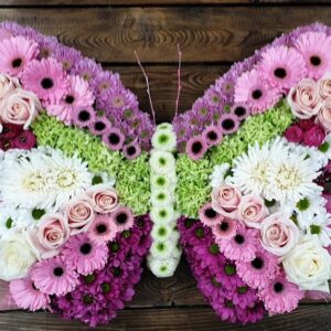 Pink and white butterfly funeral tribute made from roses, gerberas and chrysanthemums with a green centre band.