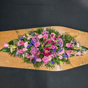 Pink lily and rose coffin spray with purple flowers on wooden coffin
