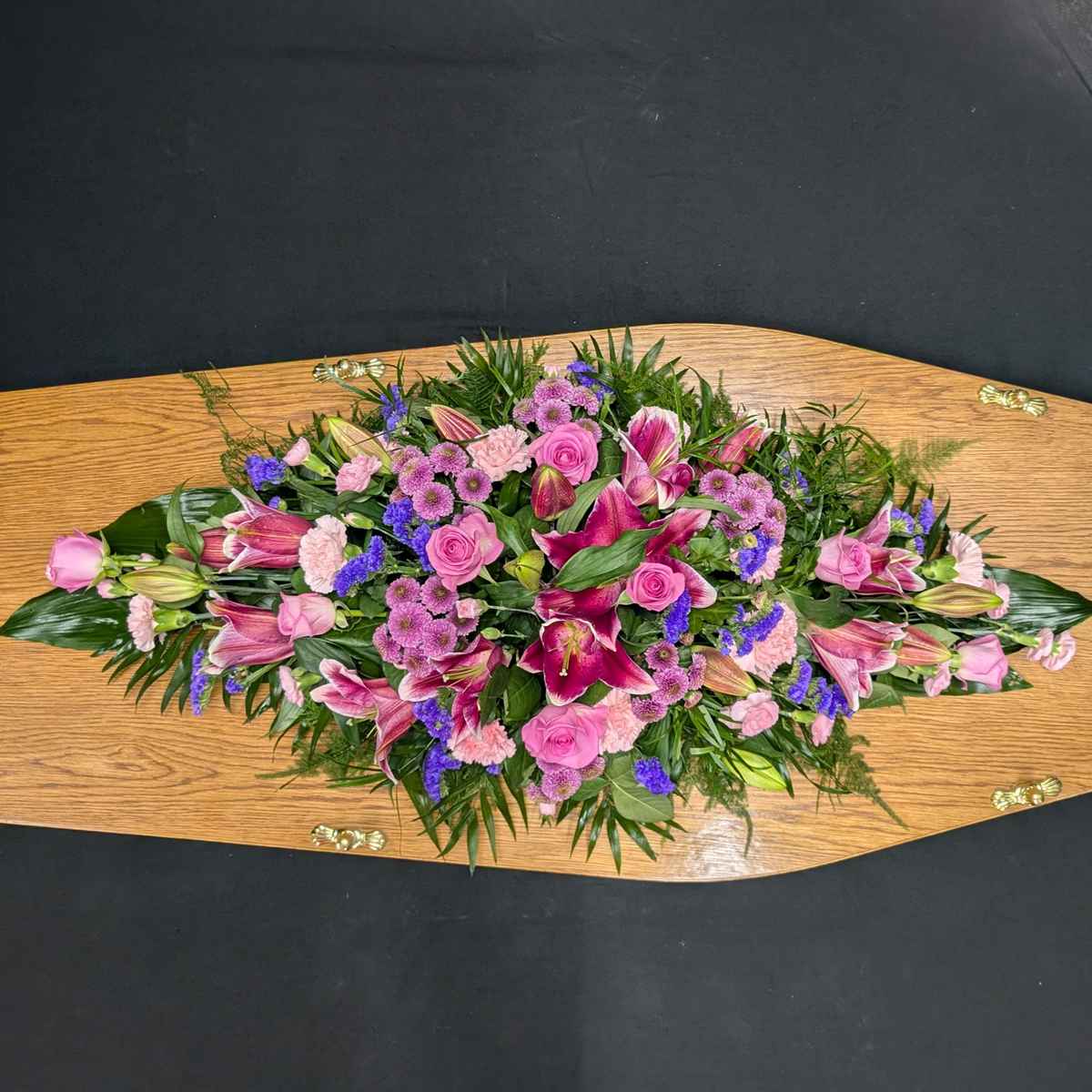 Pink lily and rose coffin spray with purple flowers on wooden coffin