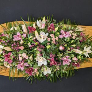 Pink orchid coffin spray with roses and lilies on wooden coffin