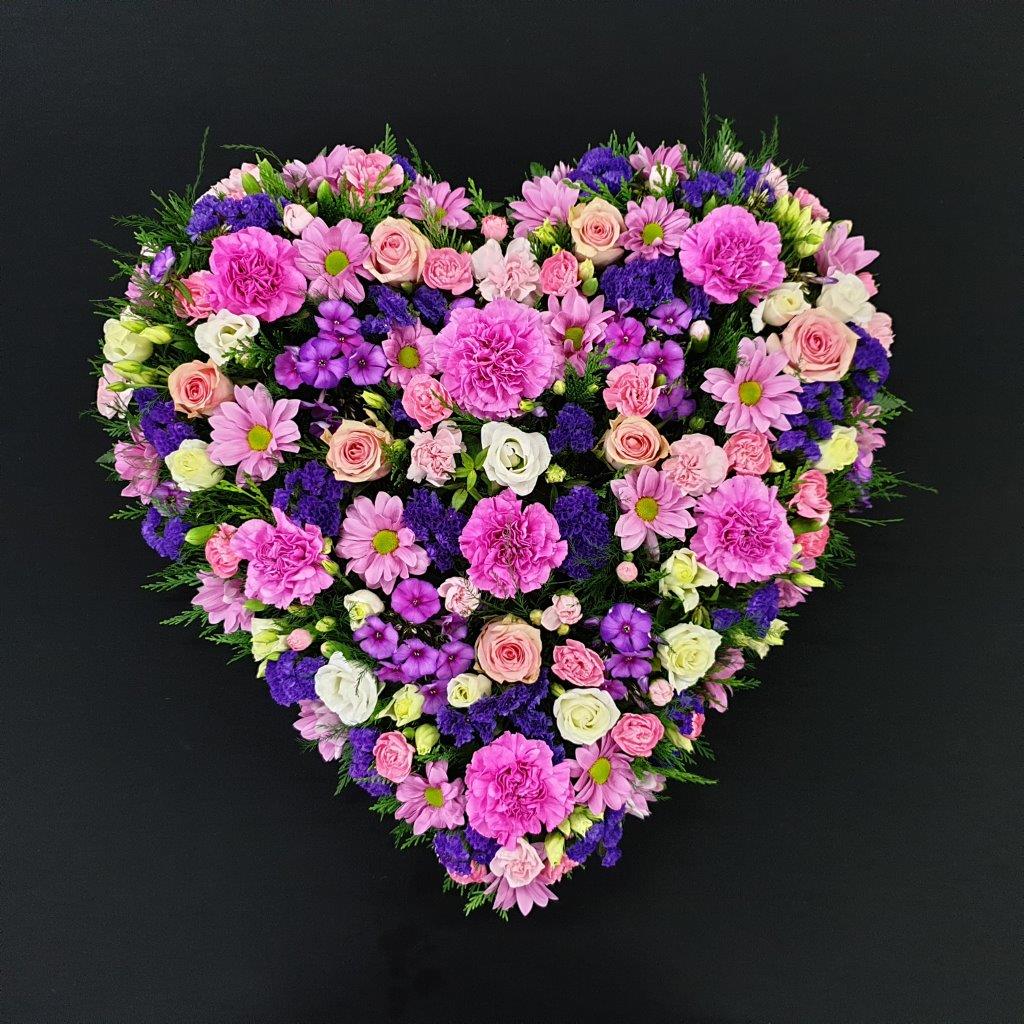 Pink and purple luxury heart funeral tribute with mixed flowers on a black background