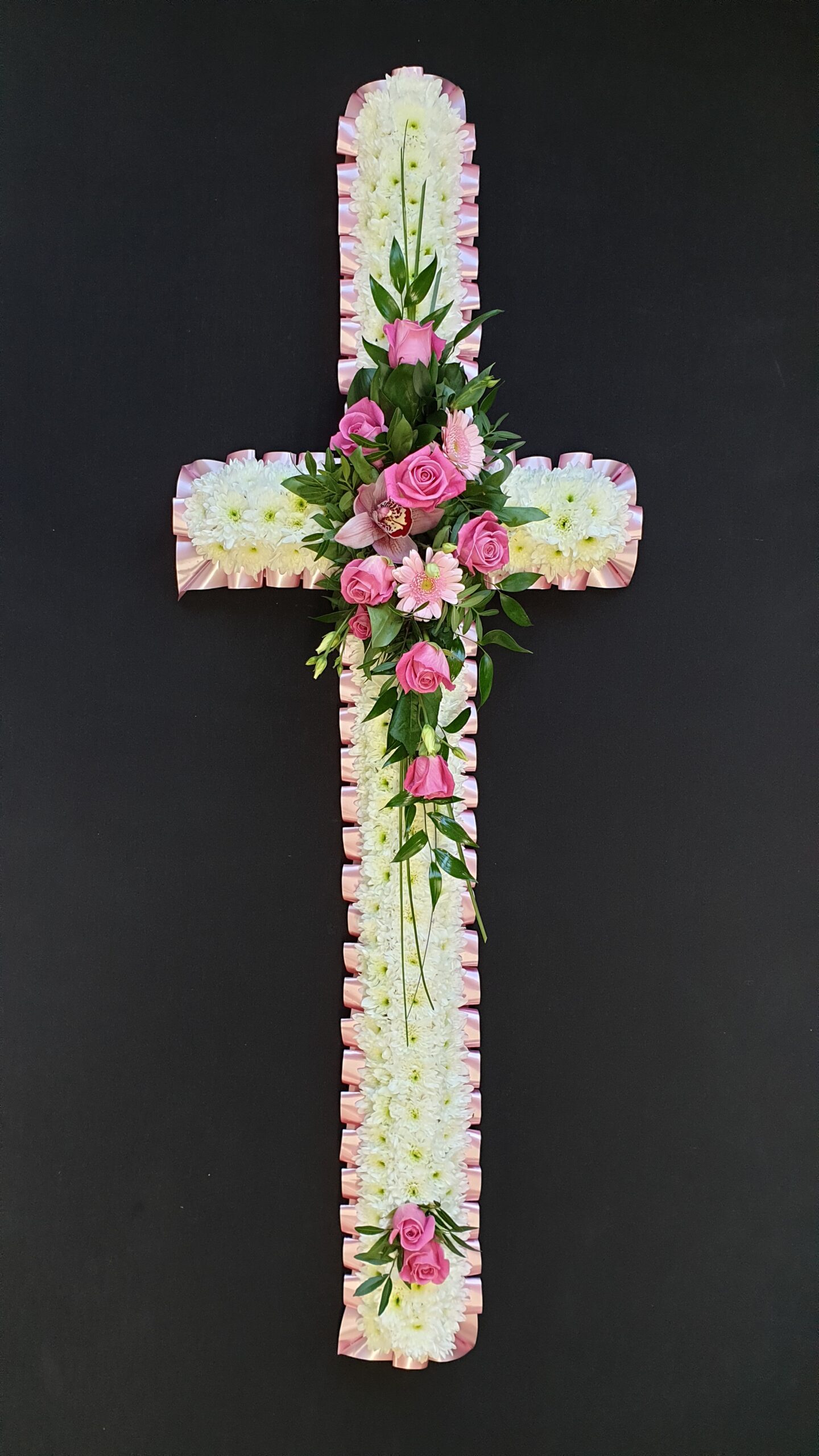 Pink and white funeral cross with chrysanthemum base, pink roses and gerberas