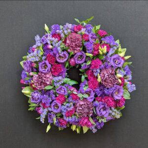 Purple and pink funeral wreath with lisianthus and carnations on a dark background
