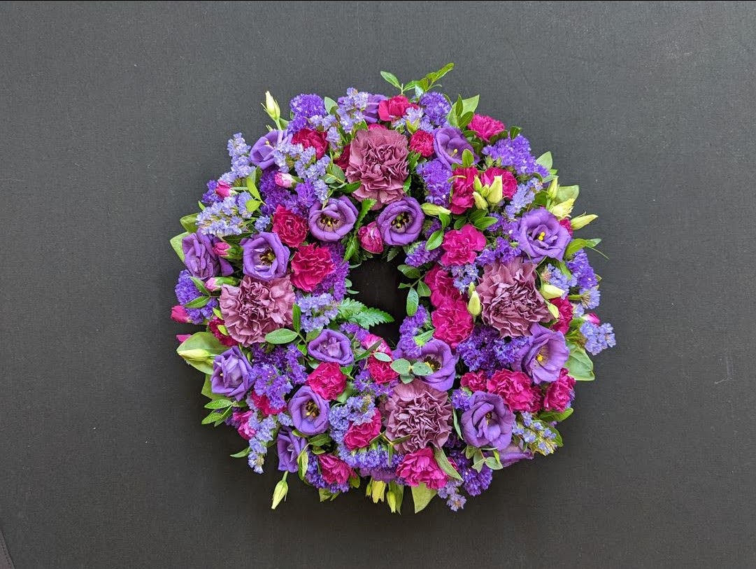 Purple and pink funeral wreath with lisianthus and carnations on a dark background