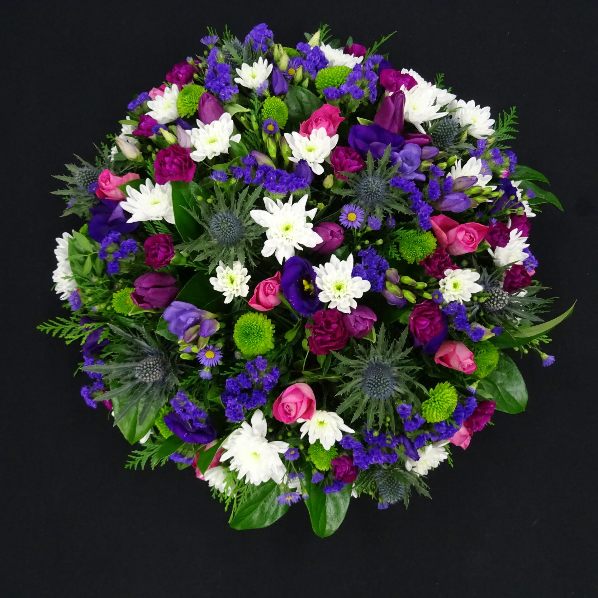 Purple and pink funeral posy with thistles, roses, lisianthus and white chrysanthemums