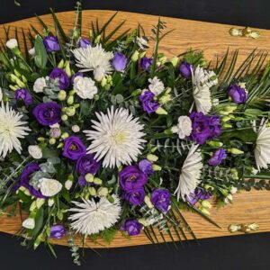Purple and white single ended funeral spray with lisianthus, chrysanthemums and carnations on a wooden coffin.