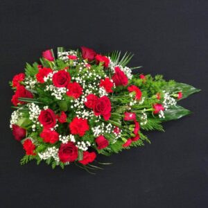 Red rose and carnation single ended funeral spray with gypsophila and greenery on a black background.