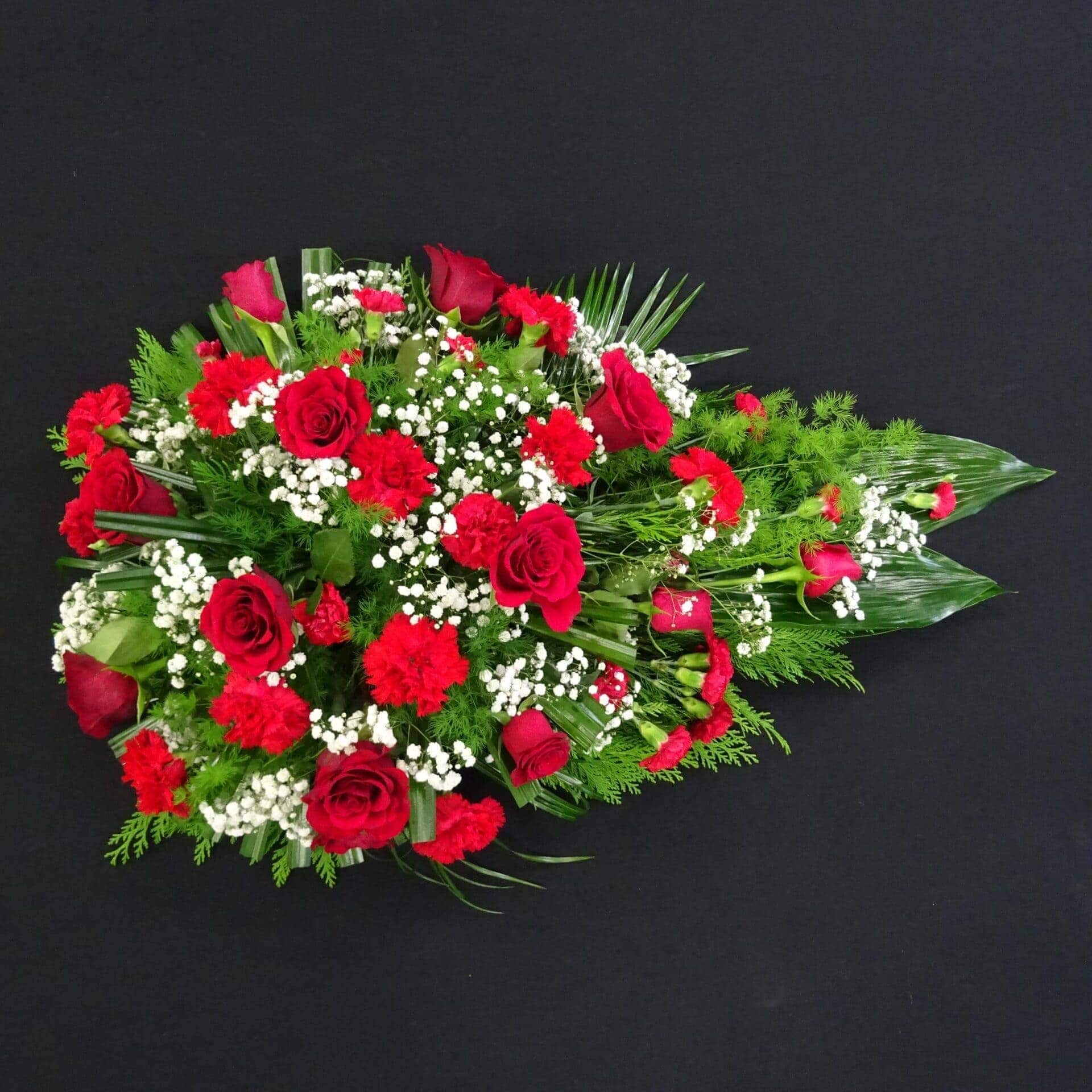 Red rose and carnation single ended funeral spray with gypsophila and greenery on a black background.