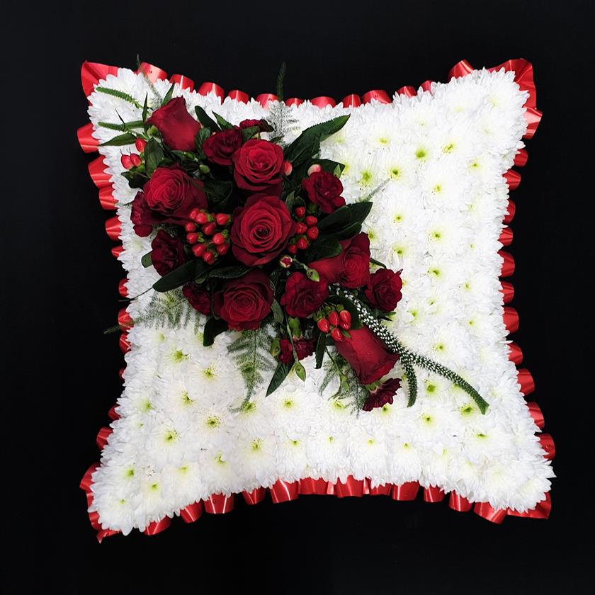 Red rose funeral cushion tribute with white chrysanthemum base and red ribbon edge