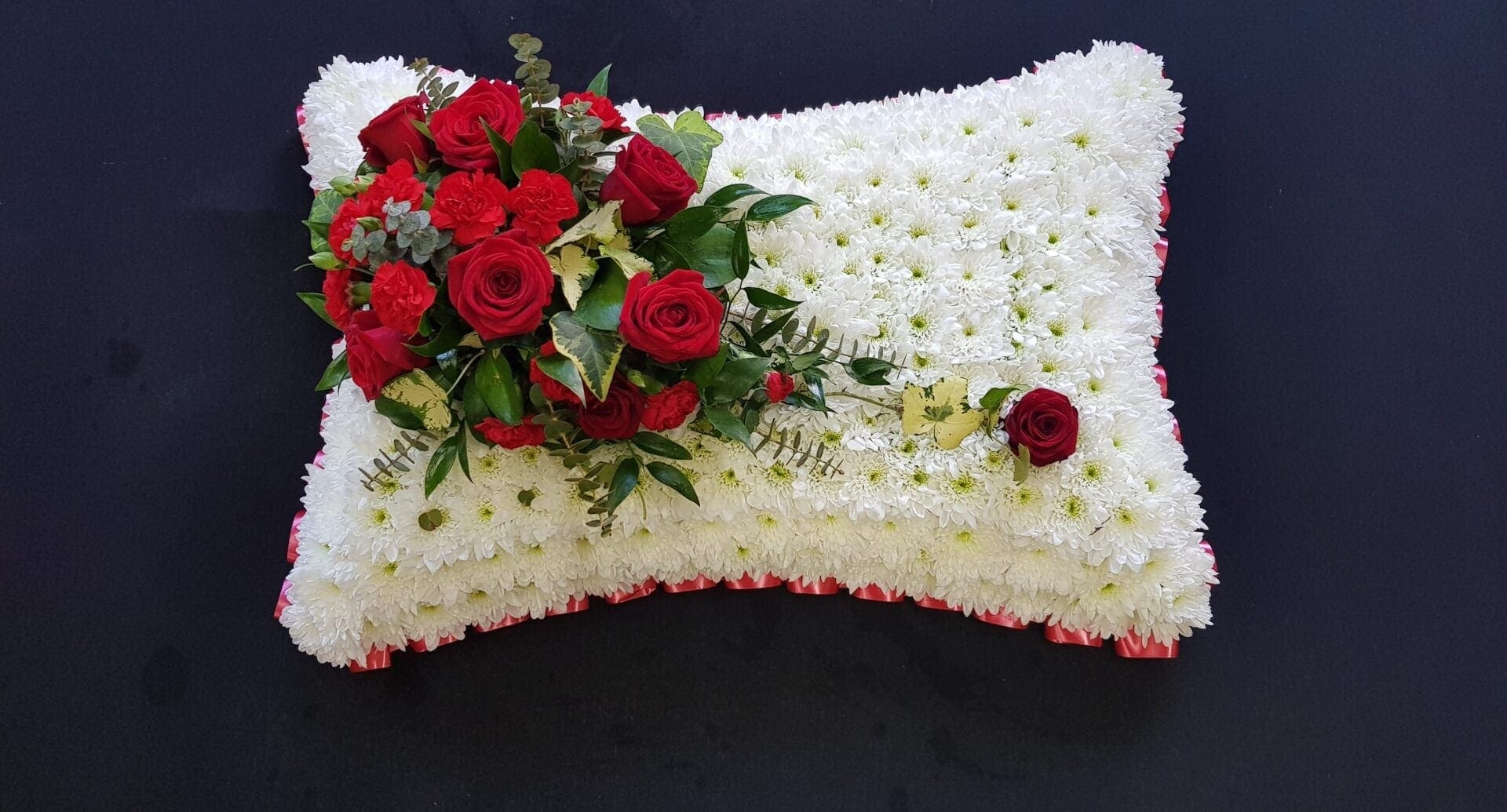Red rose funeral pillow tribute with white chrysanthemum base and red ribbon edge