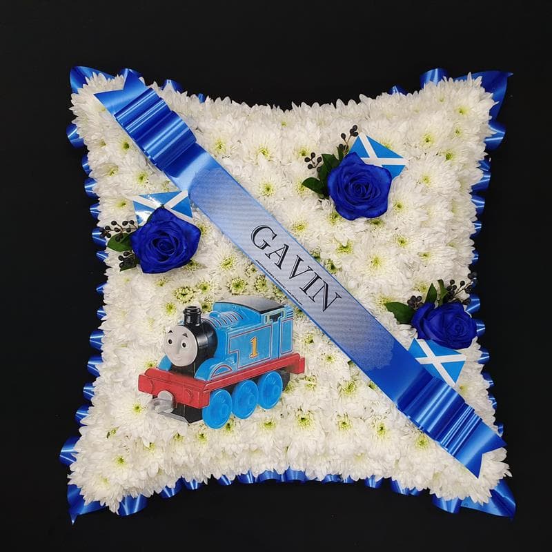 Children’s train-themed funeral cushion with white chrysanthemums, blue roses, Scottish flags and personalised blue name ribbon.