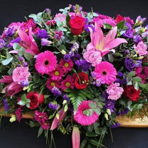 Bright pink and purple coffin spray with lilies, gerberas and roses on wooden coffin