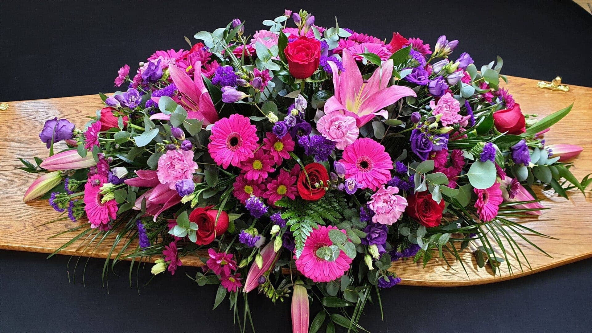 Bright pink and purple coffin spray with lilies, gerberas and roses on wooden coffin