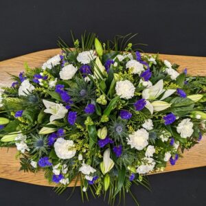 White and blue coffin spray with lilies, carnations and thistles on wooden coffin