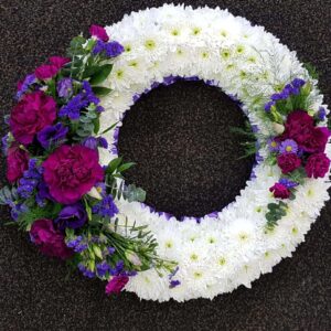 White based funeral wreath with purple ribbon edge and rich purple flower sprays